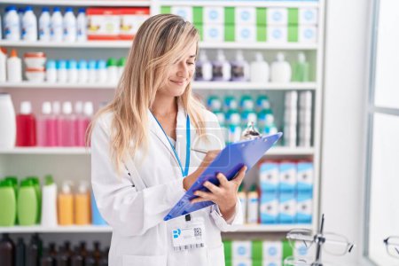 Photo for Young blonde woman pharmacist writing on document at pharmacy - Royalty Free Image