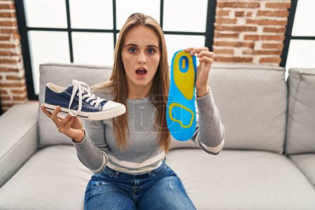 Photo for Young woman holding shoe insole in shock face, looking skeptical and sarcastic, surprised with open mouth - Royalty Free Image