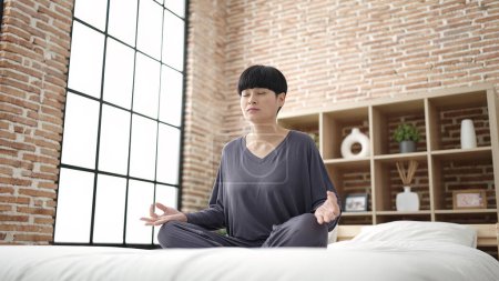 Photo for Young chinese woman doing yoga exercise sitting on bed at bedroom - Royalty Free Image