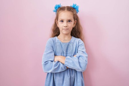 Photo for Young little girl standing over pink background skeptic and nervous, disapproving expression on face with crossed arms. negative person. - Royalty Free Image