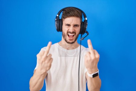 Foto de Hispanic man with beard listening to music wearing headphones showing middle finger doing fuck you bad expression, provocation and rude attitude. screaming excited - Imagen libre de derechos