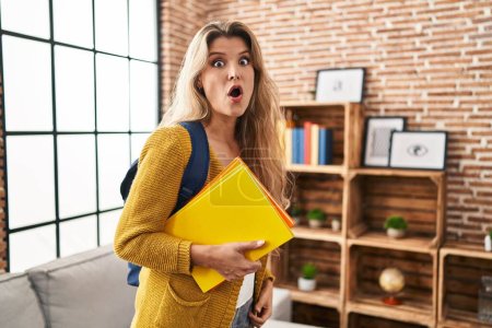 Photo for Young woman wearing student backpack and holding books scared and amazed with open mouth for surprise, disbelief face - Royalty Free Image
