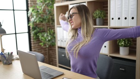 Foto de Joven mujer rubia trabajadora de negocios usando portátil estirando brazos en la oficina - Imagen libre de derechos