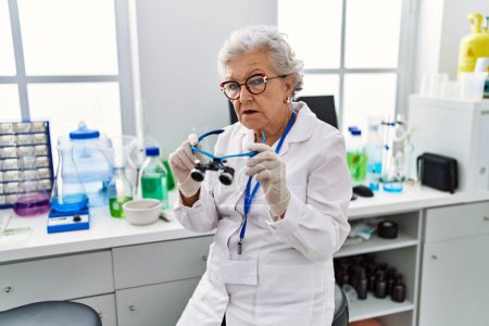 Photo for Senior woman with grey hair working at scientist laboratory using magnifying glasses relaxed with serious expression on face. simple and natural looking at the camera. - Royalty Free Image