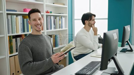 Foto de Dos hombres estudiantes usando libro de lectura por computadora estudiando en la universidad de la biblioteca - Imagen libre de derechos