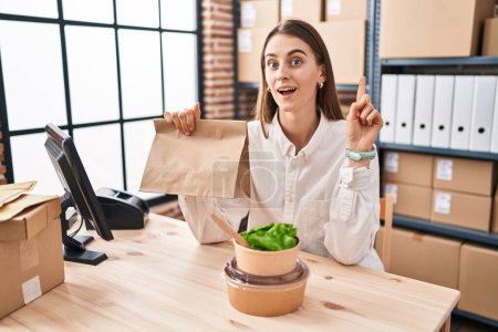Photo for Young caucasian woman working at small business ecommerce holding take away food surprised with an idea or question pointing finger with happy face, number one - Royalty Free Image