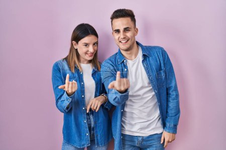 Téléchargez les photos : Jeune couple hispanique debout sur fond rose signe venir ici geste avec la main invitant accueillant heureux et souriant - en image libre de droit