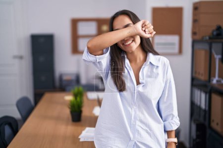 Photo for Young hispanic woman at the office covering eyes with arm smiling cheerful and funny. blind concept. - Royalty Free Image