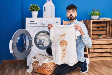 Photo for Young hispanic man with beard holding clean white t shirt and t shirt with dirty stain puffing cheeks with funny face. mouth inflated with air, catching air. - Royalty Free Image