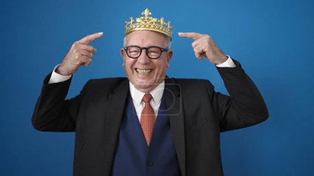Photo for Senior business man wearing crown over isolated blue background - Royalty Free Image
