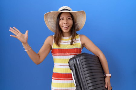 Foto de Mujer china de mediana edad sosteniendo la maleta que va de vacaciones de verano celebrando la victoria con sonrisa feliz y la expresión ganadora con las manos levantadas - Imagen libre de derechos