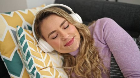 Young blonde woman listening to music relaxing on sofa at home