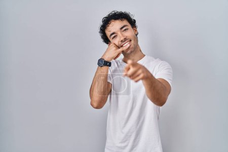 Téléchargez les photos : Homme hispanique debout sur fond isolé souriant faire parler au téléphone geste et vous pointant du doigt. Appelle-moi. - en image libre de droit