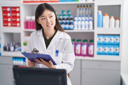 Photo for Chinese woman pharmacist writing on document at pharmacy - Royalty Free Image