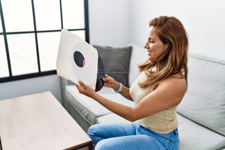 Téléchargez les photos : Jeune femme latine souriant confiant tenant disque de vinyle à la maison - en image libre de droit