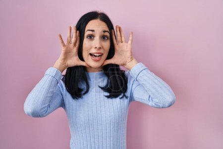 Téléchargez les photos : Hispanic woman standing over pink background smiling cheerful playing peek a boo with hands showing face. surprised and exited - en image libre de droit