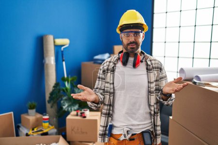 Photo for Young hispanic man with beard working at home renovation clueless and confused with open arms, no idea concept. - Royalty Free Image