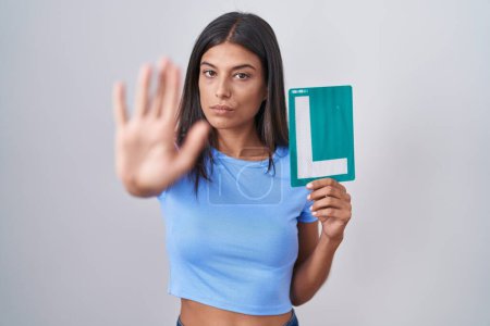 Photo for Brunette young woman holding l sign for new driver with open hand doing stop sign with serious and confident expression, defense gesture - Royalty Free Image