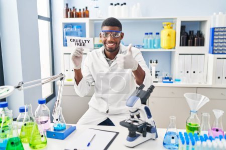 Téléchargez les photos : Homme afro-américain travaillant sur la cruauté laboratoire libre sourire heureux et positif, pouce levé faire excellent et signe d'approbation - en image libre de droit