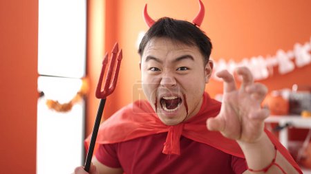 Téléchargez les photos : Jeune homme chinois portant le costume du diable faisant geste effrayant à la maison - en image libre de droit