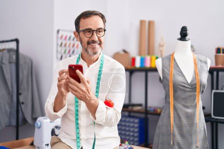 Téléchargez les photos : Middle age man tailor smiling confident using smartphone at tailor shop - en image libre de droit
