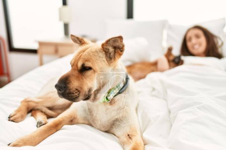 Photo for Young hispanic woman hugging dog lying on bed at bedroom - Royalty Free Image