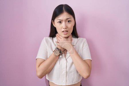 Photo for Chinese young woman standing over pink background shouting suffocate because painful strangle. health problem. asphyxiate and suicide concept. - Royalty Free Image