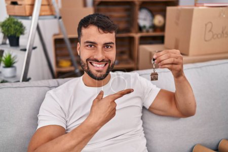 Téléchargez les photos : Bel homme hispanique tenant les clés de la nouvelle maison souriant heureux pointant avec la main et le doigt - en image libre de droit
