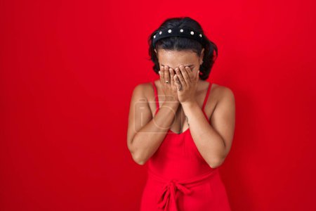 Téléchargez les photos : Jeune femme hispanique debout sur fond rouge avec une expression triste couvrant le visage avec les mains tout en pleurant. concept de dépression. - en image libre de droit