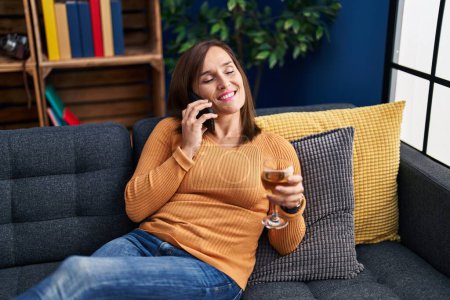 Foto de Middle age woman talking on the smartphone and drinking wine at home - Imagen libre de derechos