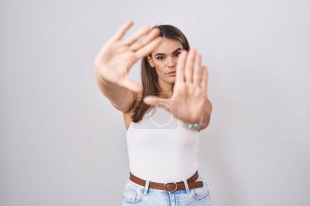 Téléchargez les photos : Jeune femme hispanique debout sur fond blanc faisant cadre en utilisant les mains paumes et les doigts, perspective de la caméra - en image libre de droit