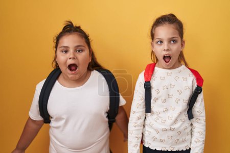 Foto de Dos niñas amigas con mochila de estudiante asustadas y sorprendidas con la boca abierta para sorpresa, cara de incredulidad - Imagen libre de derechos