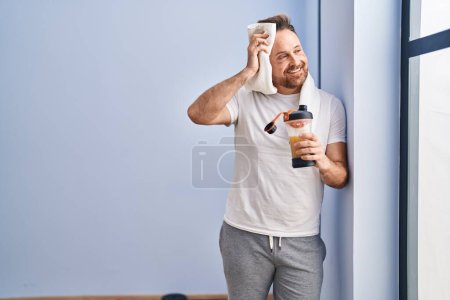 Photo for Young caucasian man drinking protein beverage using towel at sport center - Royalty Free Image