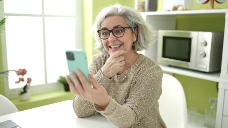 Photo for Middle age woman with grey hair using smartphone sitting on table at home - Royalty Free Image