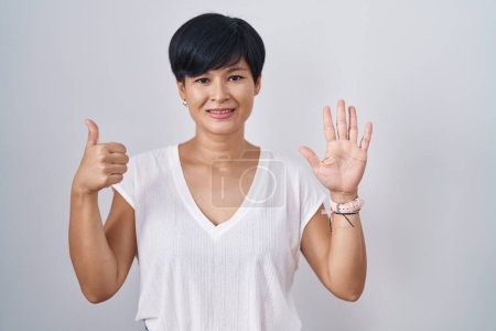 Téléchargez les photos : Jeune femme asiatique avec les cheveux courts debout sur fond isolé montrant et pointant vers le haut avec les doigts numéro six tout en souriant confiant et heureux. - en image libre de droit