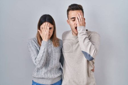 Photo for Young hispanic couple standing over white background yawning tired covering half face, eye and mouth with hand. face hurts in pain. - Royalty Free Image