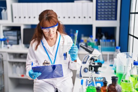 Photo for Middle age woman scientist reading report holding test tube at laboratory - Royalty Free Image