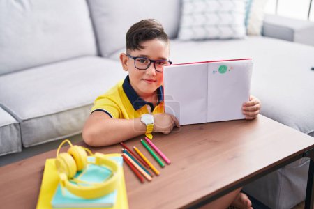 Photo for Adorable hispanic boy showing notebook with draw sitting on floor at home - Royalty Free Image