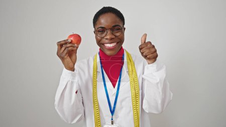 Téléchargez les photos : Femme afro-américaine diététicienne faisant pouce vers le haut tenant pomme sur fond blanc isolé - en image libre de droit