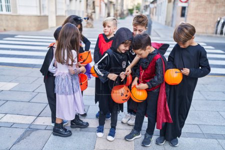 Téléchargez les photos : Groupe d'enfants portant un costume d'Halloween mettant des bonbons dans le panier de citrouille à la rue - en image libre de droit