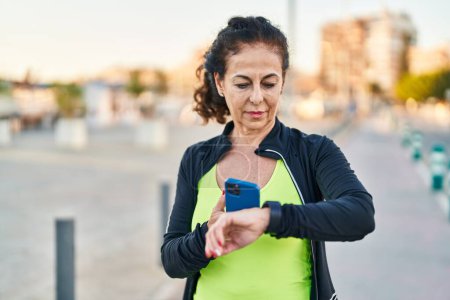 Téléchargez les photos : Middle age hispanic woman working out with smart watch outdoors - en image libre de droit