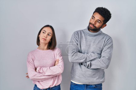 Photo for Young hispanic couple standing together looking to the side with arms crossed convinced and confident - Royalty Free Image