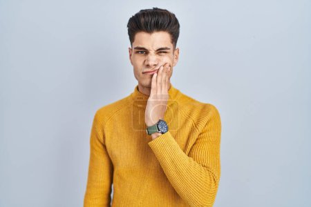 Photo for Young hispanic man standing over blue background touching mouth with hand with painful expression because of toothache or dental illness on teeth. dentist - Royalty Free Image