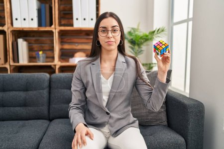 Foto de Mujer hispana jugando colorido rompecabezas cubo inteligencia juego pensamiento actitud y expresión sobria buscando confianza en sí mismo - Imagen libre de derechos