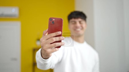 Téléchargez les photos : Jeune homme hispanique faire selfie par caméra debout à la maison - en image libre de droit
