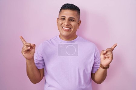 Téléchargez les photos : Young hispanic man standing over pink background smiling confident pointing with fingers to different directions. copy space for advertisement - en image libre de droit