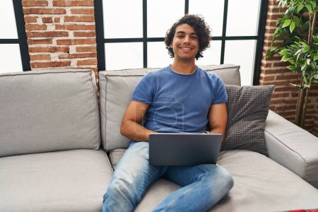 Téléchargez les photos : Young hispanic man using laptop sitting on sofa at home - en image libre de droit