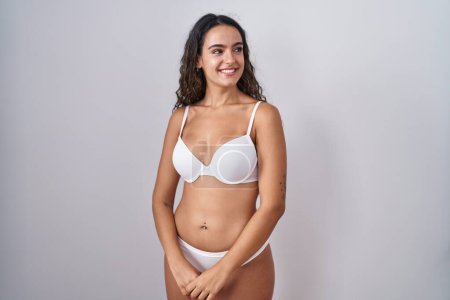 Foto de Mujer hispana joven con lencería blanca mirando hacia otro lado con sonrisa en la cara, expresión natural. riendo confiado. - Imagen libre de derechos