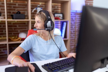 Photo for Young caucasian woman playing video games wearing headphones looking to side, relax profile pose with natural face and confident smile. - Royalty Free Image