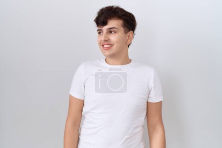Téléchargez les photos : Jeune homme non binaire portant t-shirt blanc décontracté regardant de côté avec le sourire sur le visage, expression naturelle. riant confiant. - en image libre de droit